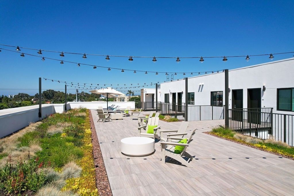 A patio with a white table and chairs is surrounded by a fence and has a string of lights above it.