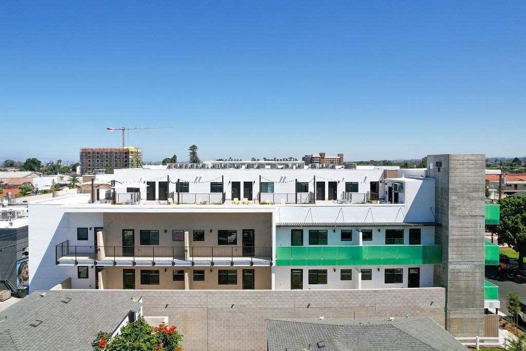 A white building with a green stripe on the side is under construction with a crane in the background.