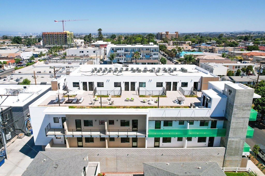 A large white building with a green stripe on the side is surrounded by other buildings.
