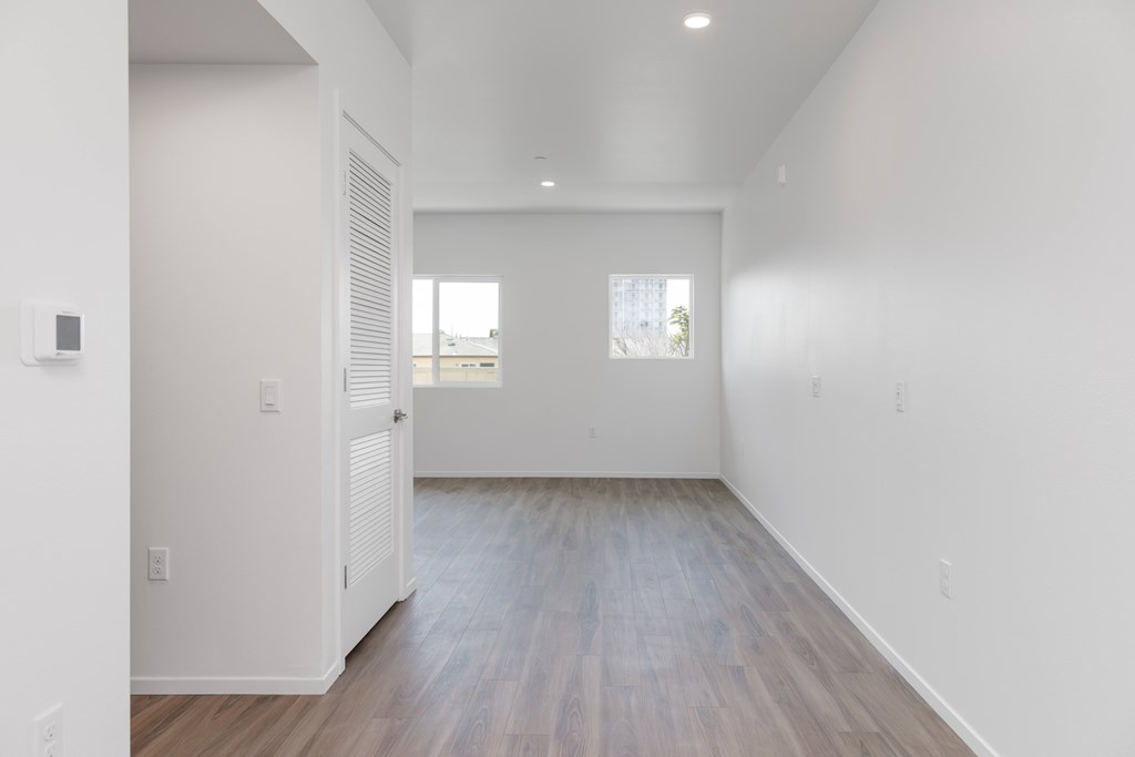 A room with white walls and wooden flooring with a window.