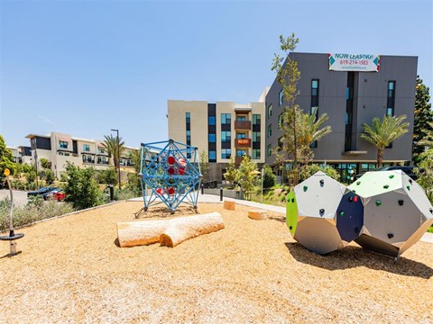 A playground with a climbing structure and a building in the background.
