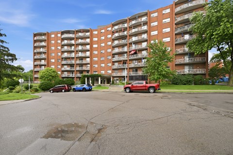 A red truck is parked in a parking lot in front of a large apartment building.