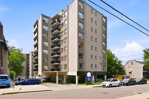 A tall apartment building with a blue car parked in front.