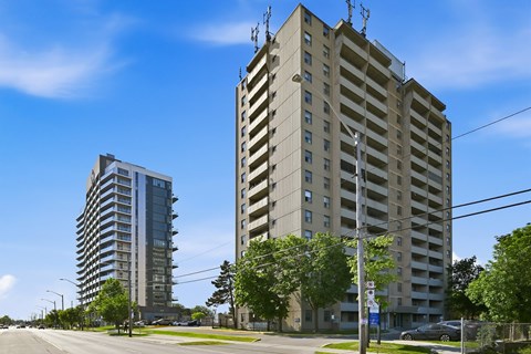 A tall building with a flat roof and a balcony on the top floor stands next to a shorter building with a curved roof.