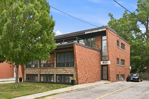 A black car is parked in front of a brick building with the number 70 on it.