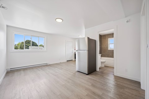 A spacious, empty room with a white fridge and wooden flooring.