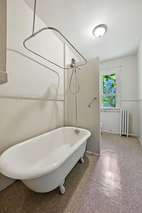 A white bathtub with a shower head and a window in the bathroom.