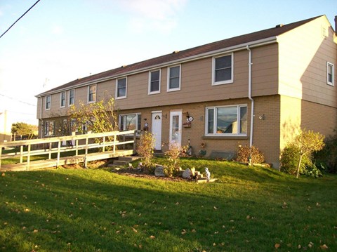 A house with a brown and beige exterior has a white door and a small porch.