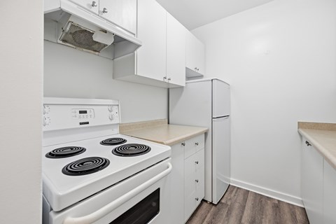 A white stove with four burners is in a kitchen with white cabinets.