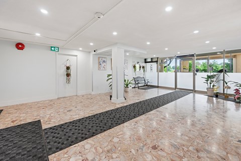 A hallway with a marble floor and a red fire alarm on the wall.