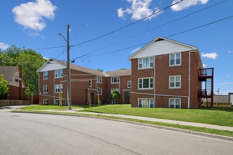 A red brick apartment building with a white roof and a balcony on the second floor.