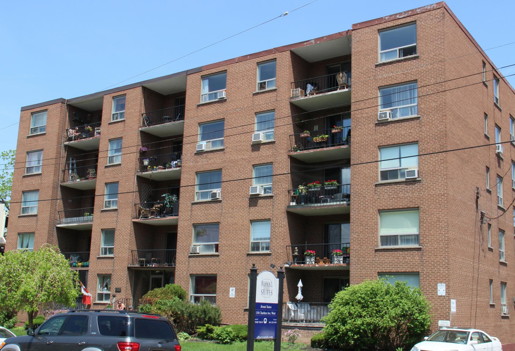 A large brick building with balconies and cars parked in front.