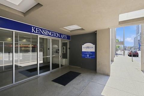 The image shows the entrance to Kensington Apartments with a blue signboard and a glass door.