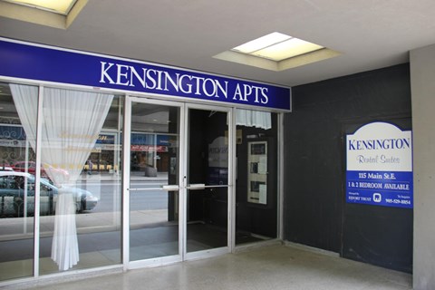 The image shows the front of Kensington Apts with a blue signboard and a window with white curtains.