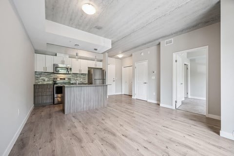A spacious, empty room with wooden flooring and a kitchen area in the background.