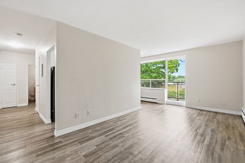 A spacious room with wooden flooring and a view of trees through the window.