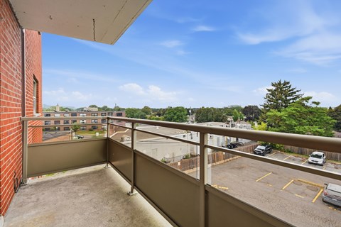 A balcony with a view of a parking lot and trees.