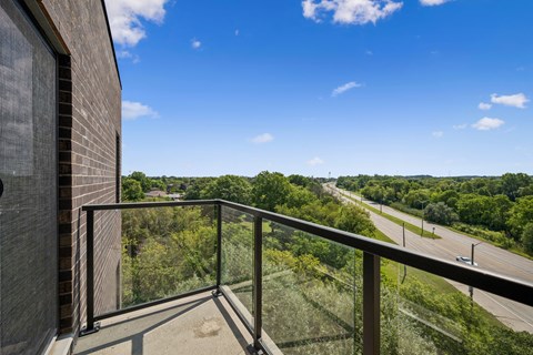 A balcony with a glass railing overlooks a highway and trees.