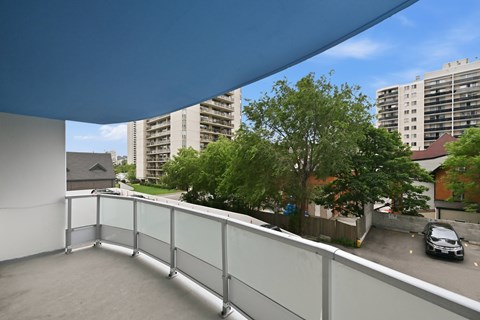 A balcony with a glass railing overlooks a parking lot and buildings.