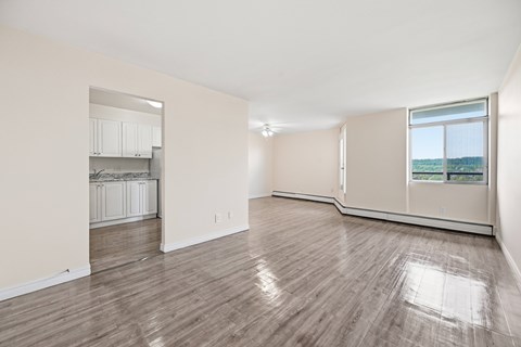 A spacious room with wooden flooring and a kitchen area in the background.