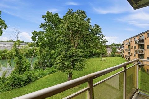 A balcony overlooks a green lawn and a body of water.