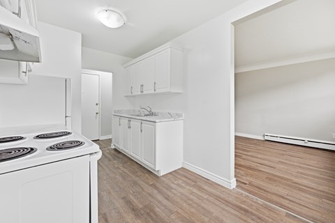 A white kitchen with a stove top oven and wooden flooring.