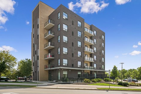 A modern apartment building with balconies and a black fence in front.