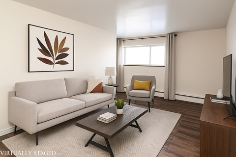 A living room with a grey couch, a yellow pillow, a brown coffee table, a lamp, a television, and a plant.