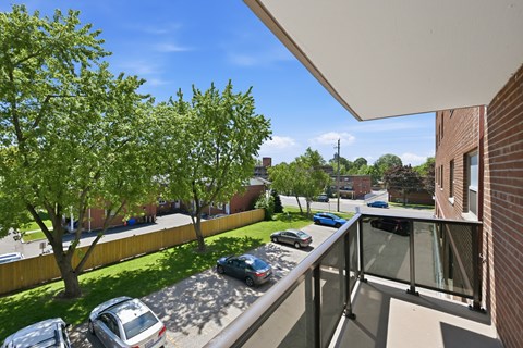 A balcony overlooks a parking lot and a tree-lined street.