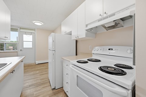 A white stove with four burners is in a kitchen with white cabinets.