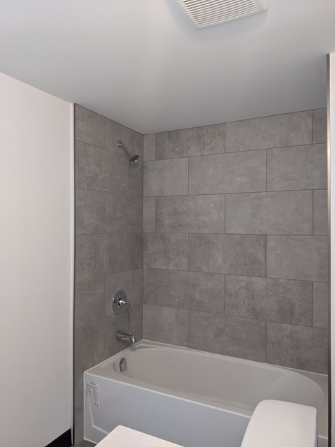 A white bathtub with a grey tile wall behind it.