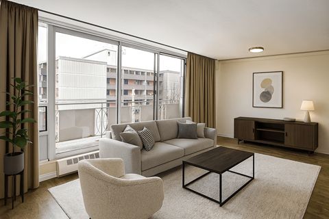 A living room with a grey couch, a white chair, a brown coffee table, and a large window with a view of a building outside.