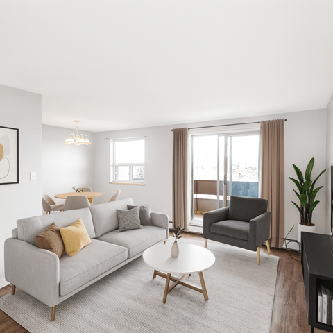 A living room with a grey couch, a grey armchair, a white coffee table, and a large window with curtains.