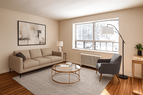 A living room with a beige couch, a grey armchair, a glass coffee table, and a framed artwork on the wall.