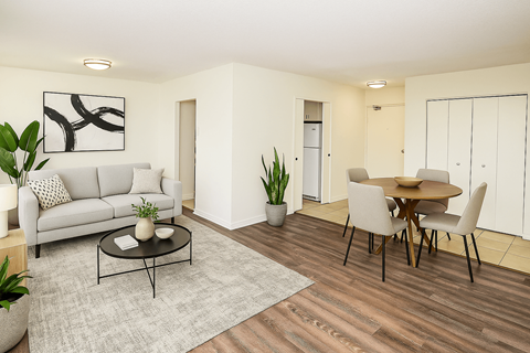 A living room with a grey couch, a coffee table, a dining table with chairs, and a plant.