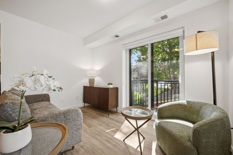 A living room with a grey couch, a green armchair, a wooden coffee table, and a white vase with white flowers.