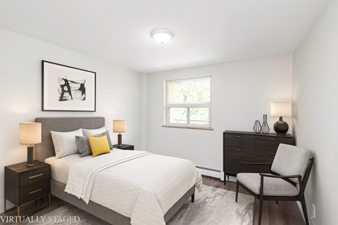 A bedroom with a bed, chair, and a picture on the wall.