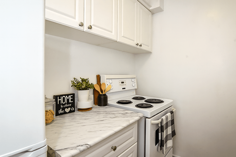 A white kitchen with a stove and a sign that says "home is where the heart is".