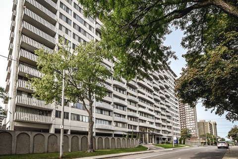 A tall residential building with balconies is surrounded by trees.