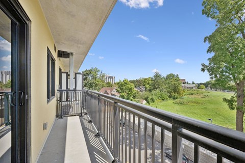 A balcony with a metal railing and a view of a green lawn and trees.