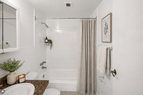 A bathroom with a white tub, a plant, and a candle on the counter.