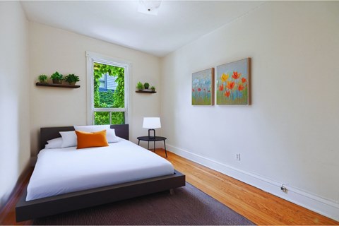 A bedroom with a bed, a window, and two paintings on the wall.