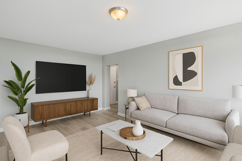 A living room with a grey couch, a white coffee table, and a large flat screen TV mounted on the wall.