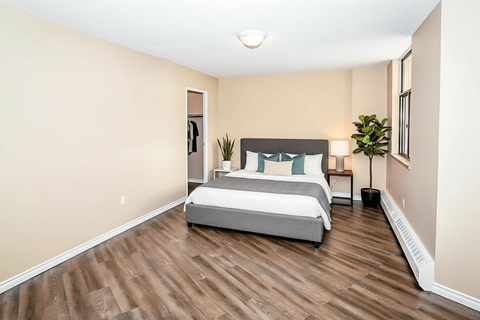 A bedroom with a bed, nightstand, and a plant.