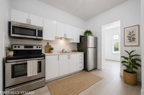 A kitchen with a stove top oven, microwave, refrigerator, and white cabinets.