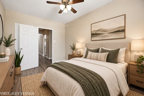 A bedroom with a bed, a ceiling fan, and a painting on the wall.