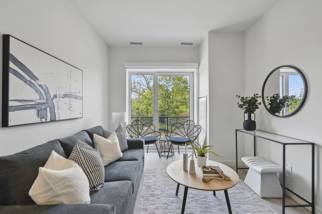 A living room with a grey couch and a round mirror on the wall at Roxy Apartments, Hamilton, ON
