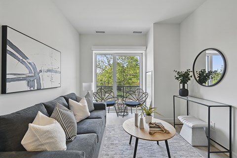 A living room with a grey couch and a round mirror on the wall.