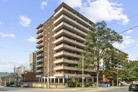 A large brown building with many windows and balconies is surrounded by trees and a street with cars.