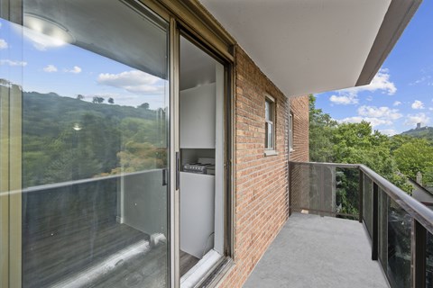 A balcony with a glass door leading to a view of a green landscape.